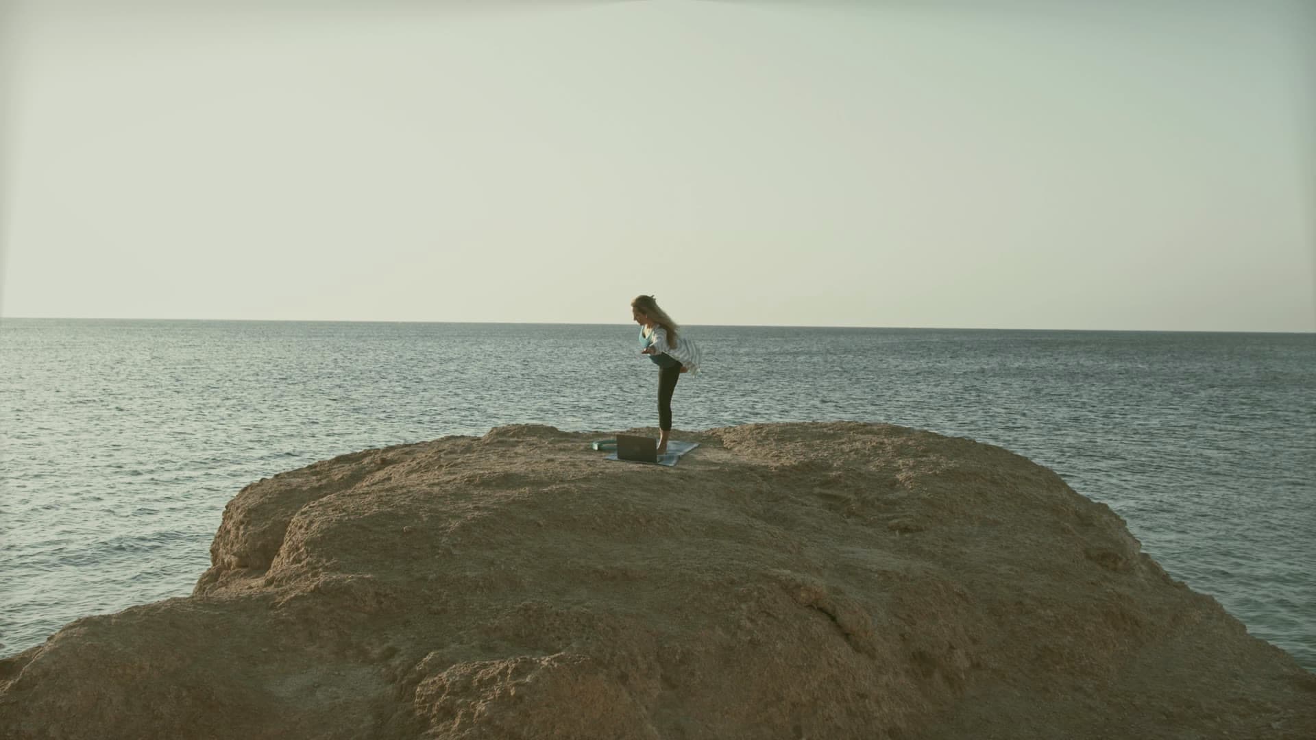 A woman stretching on a rock above the sea