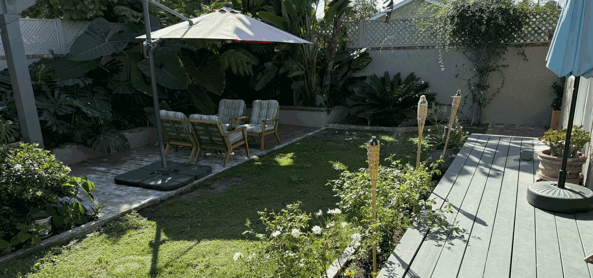 A lawn and shaded patio seen from the deck, with roses along the edge